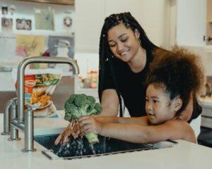 Mom and daughter washing broccoli in sink